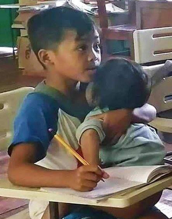 Agusan vừa bế em ngủ vừa nghe giảng và viết bài. Ảnh: Herald Hope Tero-Mangle Apole